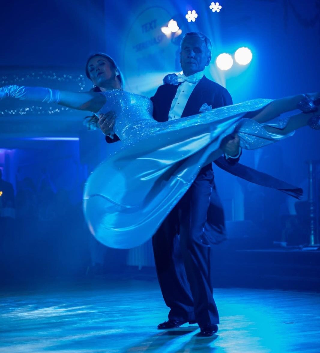 Serena dancing in a handmade Design by Gavriela dress, sweeping sparkling silver fabric as she is spun around on a dancefloor